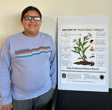 Boy with dark hair standing next to an illustration of a tobacco plant