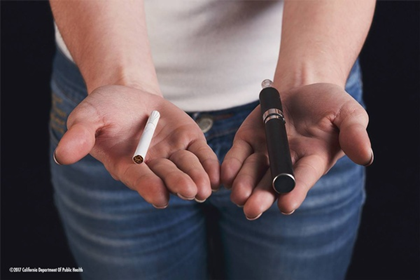 person holding a vape in one hand and a combustible cigarette in the other