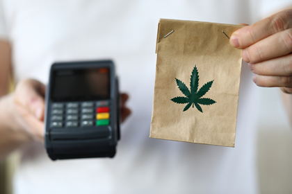 one hand holding a bag with a cannabis logo and another hand holding a credit card payment device