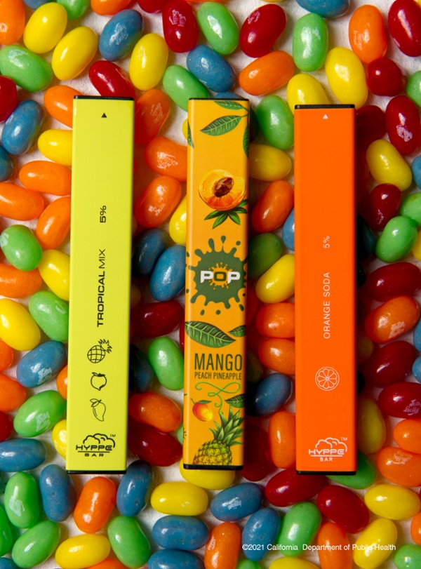 brightly colored disposable vapes lie on a bed of brightly colored jelly beans